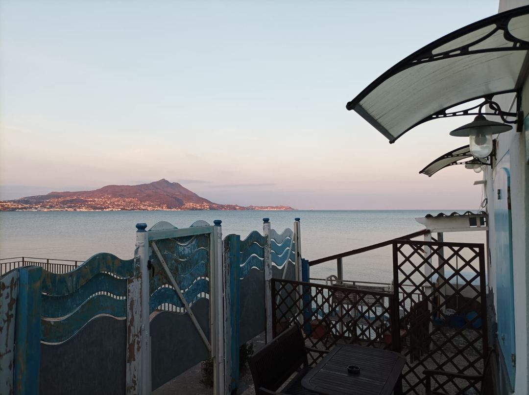 Twilight view from a beachfront terrace overlooking the Mediterranean Sea with a mountain-lined coastline dotted with lights.